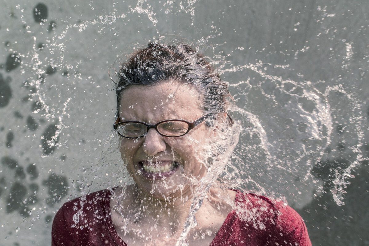 Das Bild zeigt den Kopf einer Frau mit Brille. Um den Kopf herum ist alles voller großer und kleiner Wassertropfen. Die Frau wirkt erfrischt. Das passt zu einer frischen Internetseite.